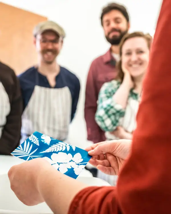Hands displaying a cyanotype artwork as participants examine the finished print